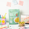 Millet Pasta package on a desk with a bowl of pasta and stationery items.
